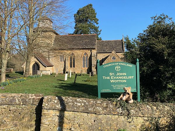 Bertie sat on a wall in front of the sign for Wotton Church, with the church in the background.
