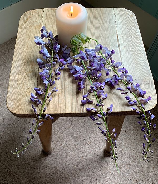 A candle lit for Diddley on a rustic table with some cut Wisteria.