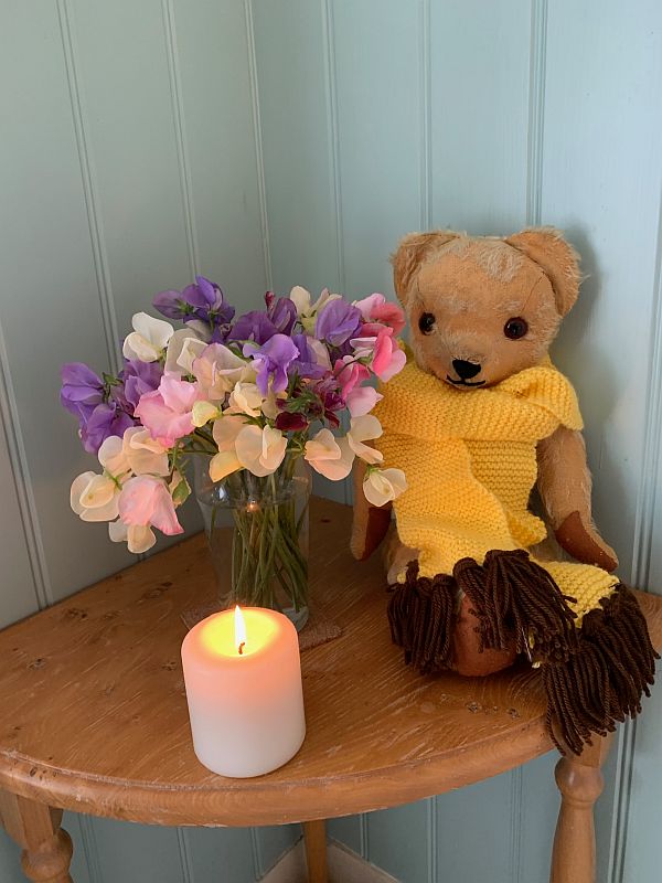 Eamonn in a yellow scarf with brown tassles next to a vase of colourful Sweet Peas. In front, a candle lit for Diddley.