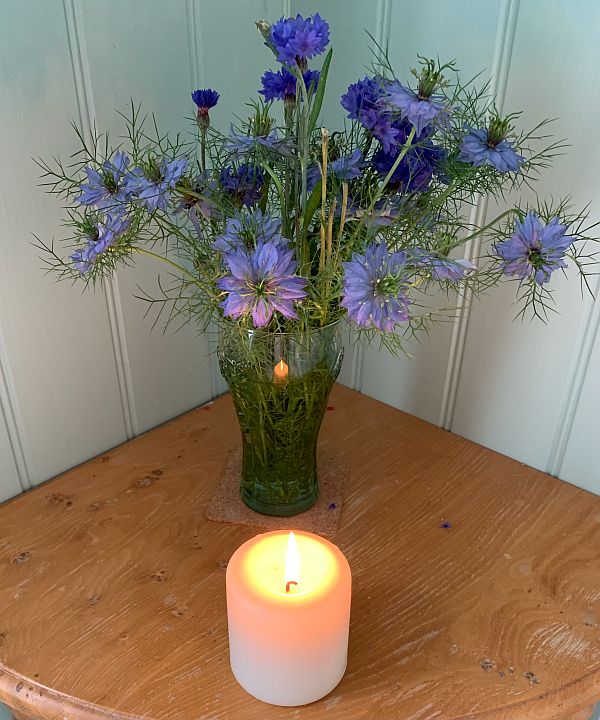 A candle lit for Diddley in front of a vase of Cornflowers.