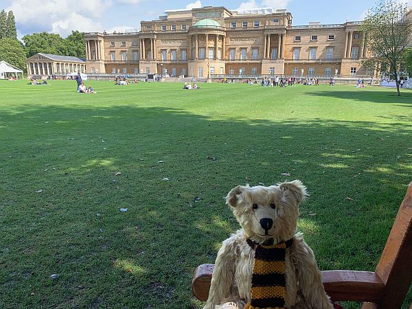 Bertie sat on a bench in the garden with the rear of Buckingham Palace in the background.