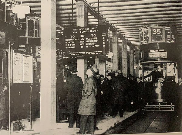 A crwoded Aldwych tram stops with at least 3 trams in view. An extensive list of destinations across London.