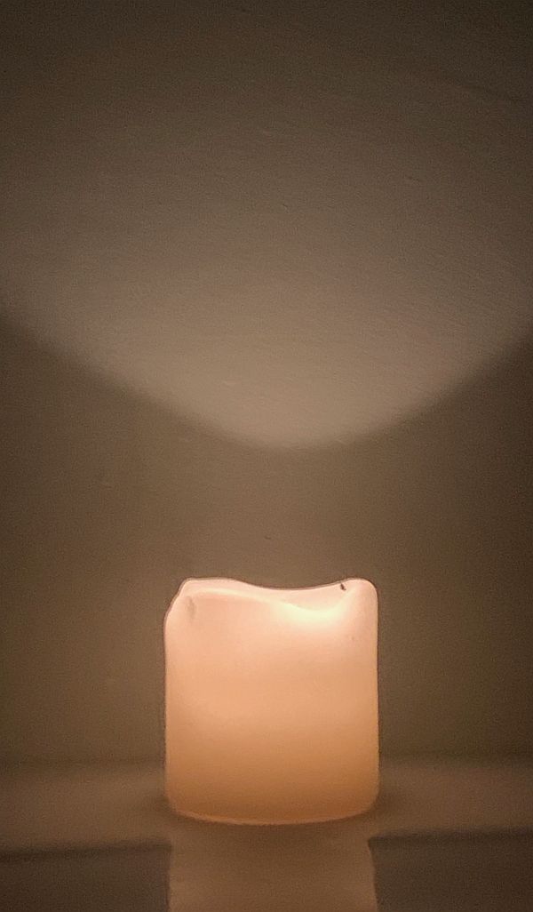 A candle lit for Diddley, reflecting against a wall.
