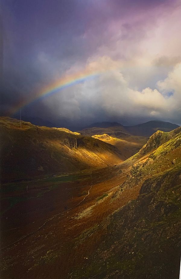 Rainbow over a cloudy hill-valley.