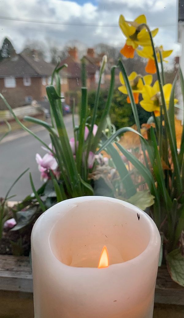 A candle lit for Diddley set against a vase of Spring flowers.