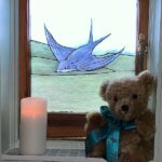Bewick the Bear with a candle lit for Diddley in front of the Bluebird window.