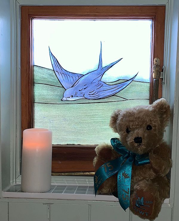 Bewick the Bear with a candle lit for Diddley in front of the Bluebird window.
