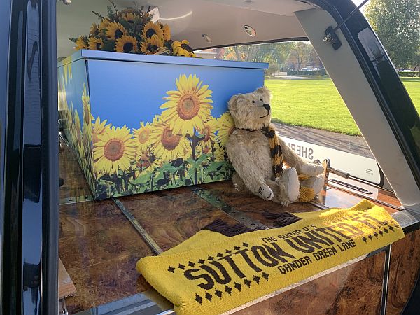 Bertie sitting against the coffin in the hearse, with a Sutton United scarf draped across the rear.