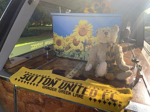 Bertie sitting against the coffin in the hearse, with a Sutton United scarf draped across the rear.