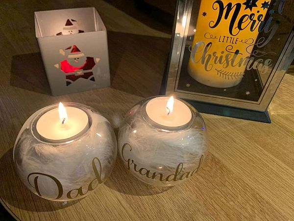 Three candles: 1 in a jar labelled "Grandad", another is a matching jar labelled "Dad" and a third in a holder with a Santa window cut into it against a much bigger candle in a glass jar with "Merry Little Christmas" etched on it.